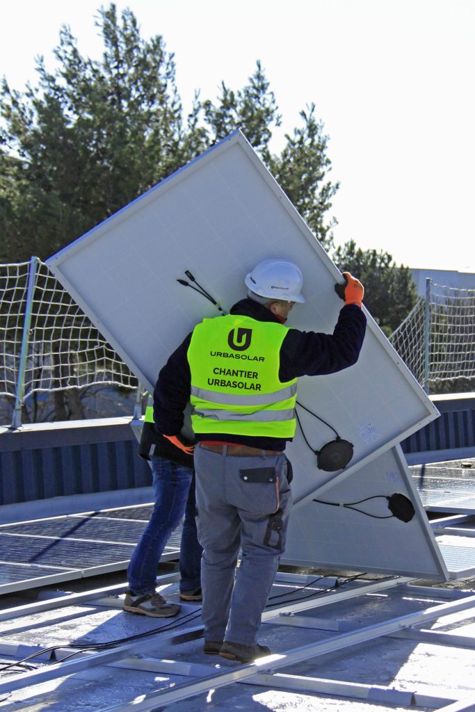 Ouvrier Urbasolar manipulant un panneau photovoltaïque sur un chantier de toiture
