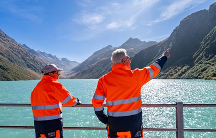 Deux collaborateurs en tenue haute visibilité observant un lac de barrage en montagne